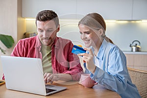 Happy wife husband spending money in online shop using laptop with credit card at home. Black Friday