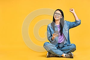 Happy winner! Business concept. Portrait of happy young woman in casual sitting on floor in lotus pose and holding mobile phone