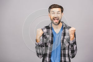 Happy winner! Happy young handsome man gesturing and keeping mouth open while standing against grey gray white background