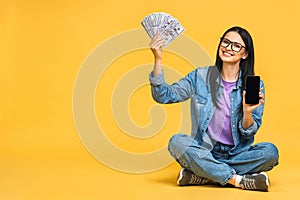 Happy winner! Portrait of a smiling cheerful woman showing blank smartphone isolated over yellow background. Sitting on the floor