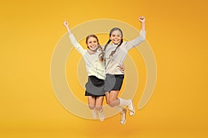 Happy winners. Little school girls jumping and making winner gestures on yellow background. Cute small winners enjoying