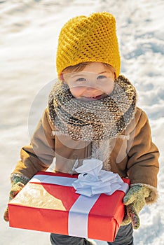 Happy winter child boy hold gift on snow background. Cute boy in winter clothes hat and scarf close up. Winter family