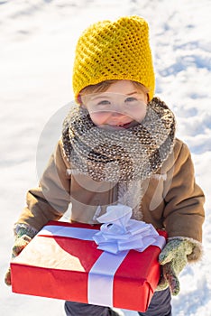 Happy winter child hold gift bow snow background. Cute boy in winter clothes hat and scarf close up. Winter holidays