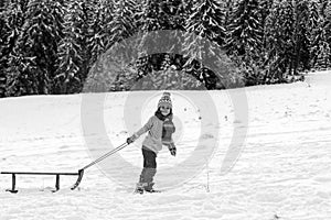 Happy winter child sledding in winter snowy forest. Kids with sled, sleigh in snow. Little boy enjoy the holiday.