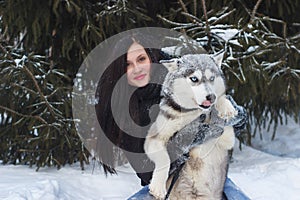 Happy winter time of joyful young woman playing with cute husky dog in snow on street.