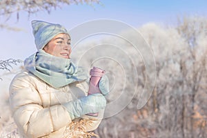 Happy winter woman holding thermo mug with hot beverage walking outdoor natural frozen park