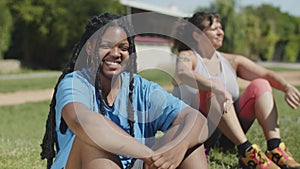 Happy woman in activewear sitting on lawn and smiling at camera