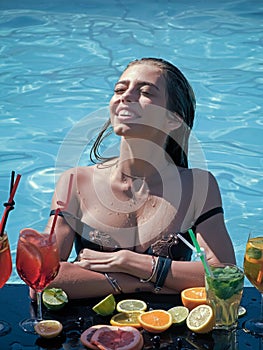 Happy woman with alcoholic beverage and fruit. Cocktail and sexy girl in pool. Summer vacation and party. Swimming and
