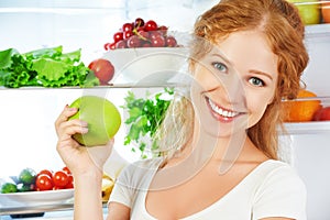 Happy woman with apple and open refrigerator with fruits, vegeta