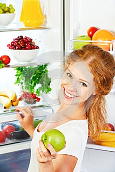 Happy woman with apple and open refrigerator with fruits, vegetables and healthy food