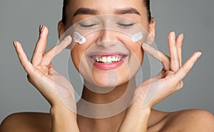 Happy Woman Applying Cosmetic Cream On Her Face