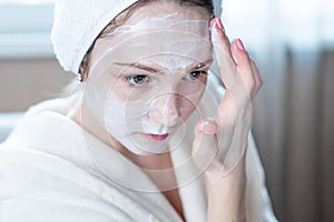 Happy woman applying cream on face moisturizing the skin. Concept of hygiene and care for the skin at home