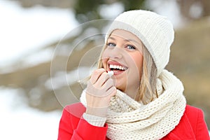 Happy woman applying lip balm outdoors in winter