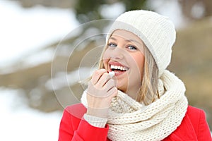 Happy woman applying lip balm outdoors in winter photo