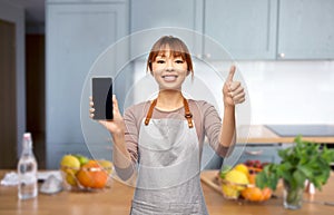 happy woman in apron showing smartphone in kitchen