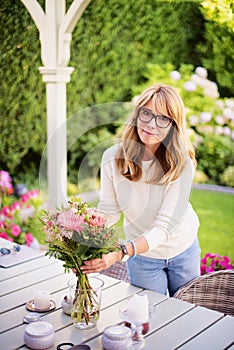 Happy woman arranging flowers in the vase on the balcony desk at home