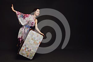 A happy woman in an Asian dress with a suitcase on a studio black ba