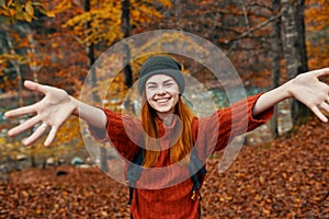 happy woman with a backpack travels in the park in autumn and gesticulate with the hands of the river in the background