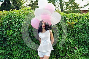 Happy woman with balloons near the green hedgerow