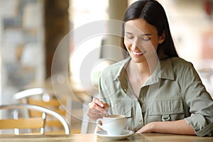 Happy woman in a bar terrace stirring coffee cup