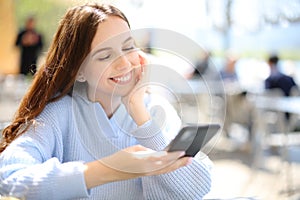 Happy woman in a bar terrace watching phone content
