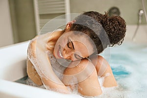 Happy woman in bathtub, smiling while bathing, barechested, leisure gesture