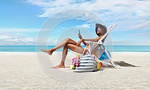 Happy woman at the beach on beach deck chair, sunbathing, uses mobile phone, in a sunny day with blue sky, concept a summer beach