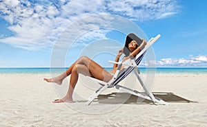 Happy woman at the beach on beach deck chair, sunbathing, wearing sun hat, in a sunny day with blue sky, concept a summer beach