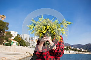 Happy woman on the beach with a bouquet of mimosa flowers.
