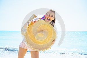 Happy woman with beach straw bag showing big hat on ocean coast