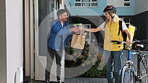 Happy woman on a bike delivering coffee and food in paper bag to customer man home. Food delivery concept.