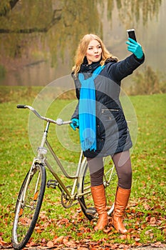 Happy woman with bike in park taking selfie photo.