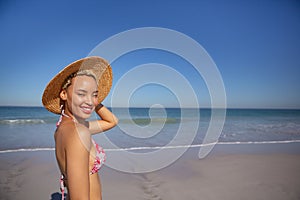 Happy woman in bikini and hat looking at camera on beach in the sunshine