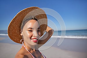 Happy woman in bikini and hat looking at camera on beach in the sunshine