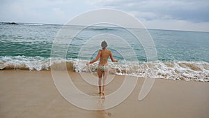 Happy woman in bikini runs towards ocean for refreshing or swimming. Young girl jogs on sand beach into the sea and