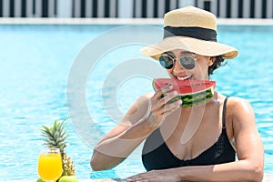 Happy woman in bikini with straw hat relaxing at swimming pool. beautiful female eats watermelon. summer time. holiday vacation co