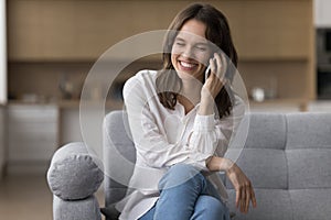 Happy young woman blab on the smartphone seated on couch photo