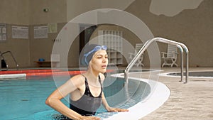 Happy woman in black swimsuit gets out of pool water