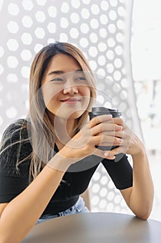 Happy woman in black t-shirt sipping hot coffee in white coffee shop.