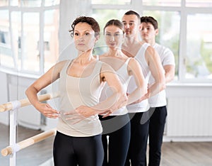 Happy woman in black and white sportswear, participating first position of ballet stance at barre with group photo