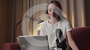 A happy woman, a blogger, recording a broadcast, putting on headphones online, talking into a microphone with an