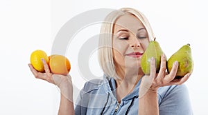 Happy woman with blond hair and beautiful smile holds two oranges, lemon and a pears in her hands for a healthy diet