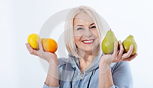 Happy woman with blond hair and beautiful smile holds two oranges, lemon and a pears in her hands for a healthy diet with