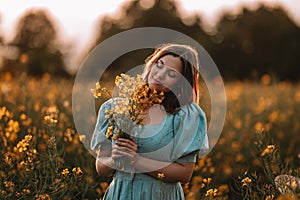 Happy woman in blooming canola flowers field. Lady in retro dress, spring season