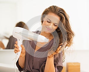 Happy woman blow drying hair in bathroom