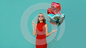 Happy woman blowing lips with bunch of red heart shaped balloons on blue background