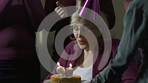 Happy woman blowing out candles on cake and making wish, 90 birthday, having fun