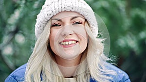 Happy woman blowing snow from palms with mittens to camera on winter forest background. Portrait of cute girl childishly