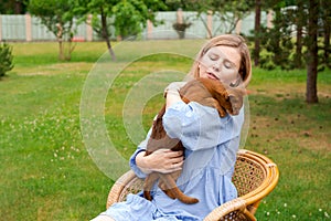 Happy woman in blue dress holding ginger imitation cat outside, outdoors