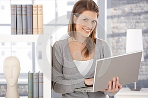 Happy woman at bookcase with computer